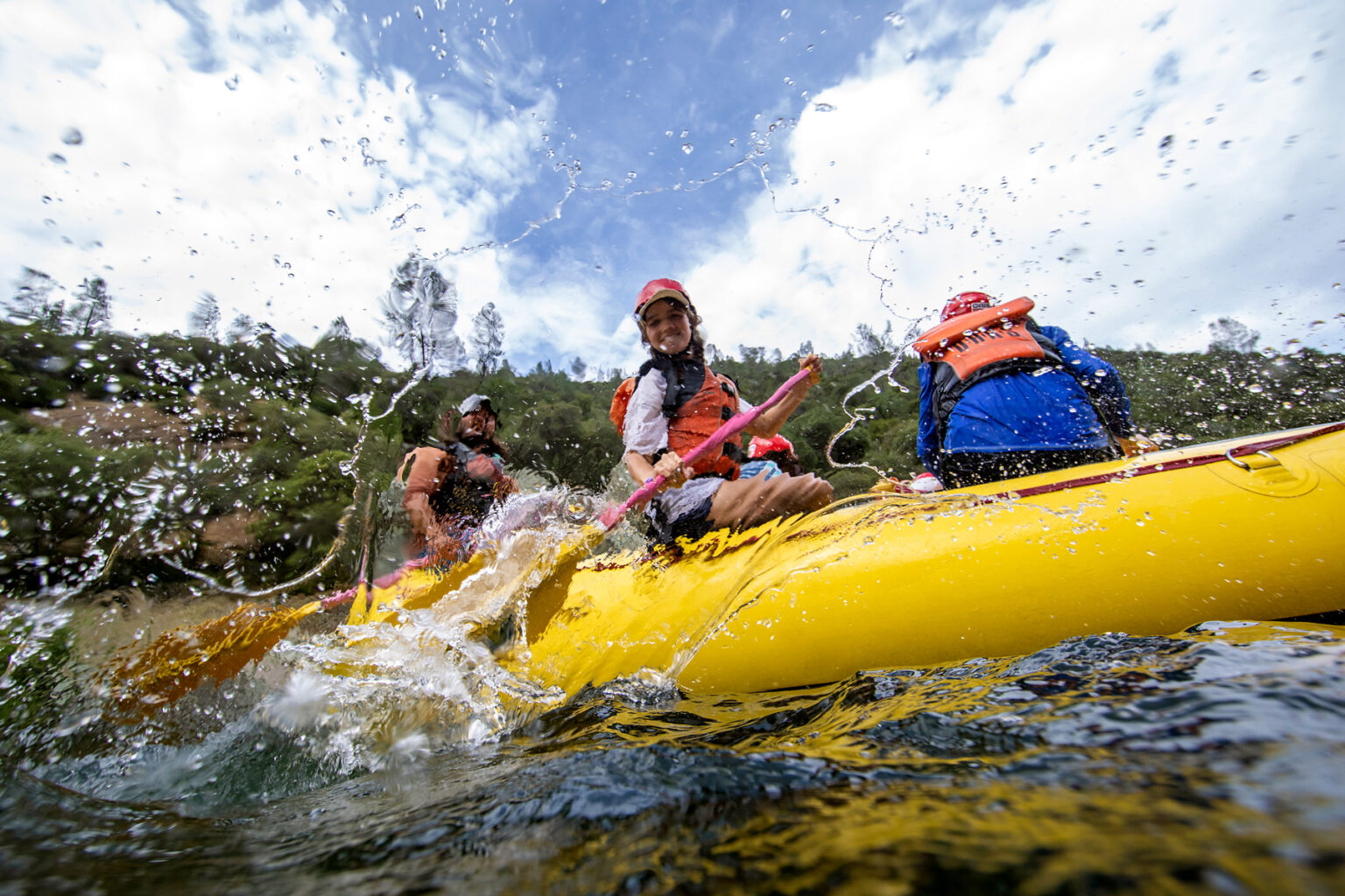 A young person splashes with a paddle during an OARS rafting trip on the South Fork of the American River.
