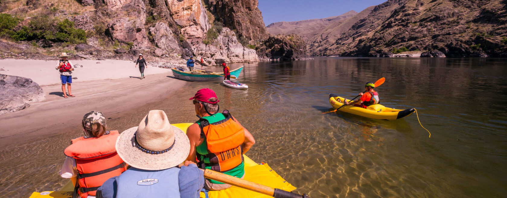 A variety of OARS boats pulling to shore on the Lower Salmon River, including an oar raft, dory, inflatable kayak and dory.