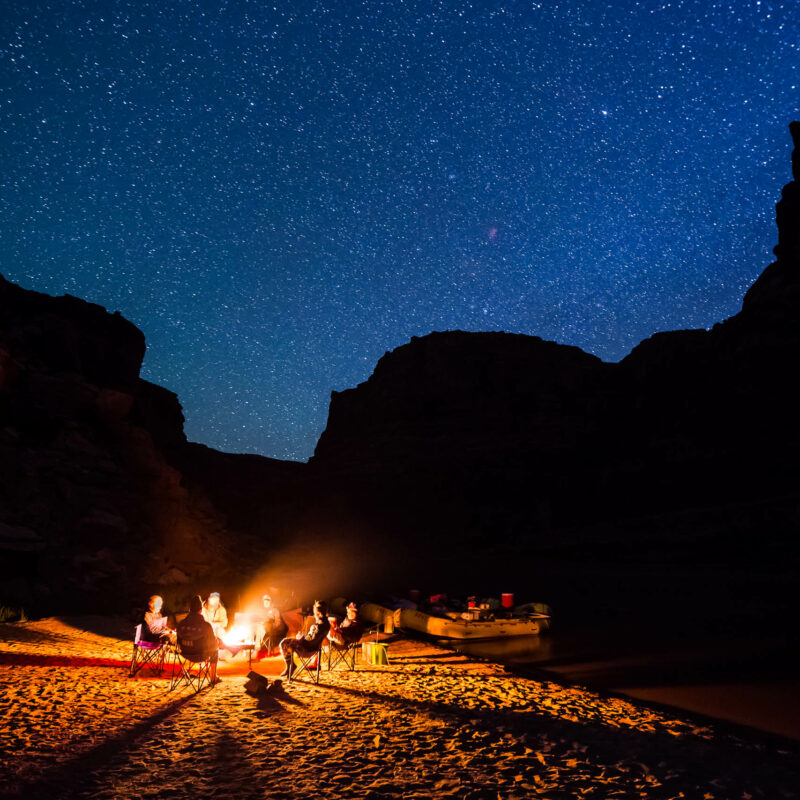 Group of travelers gathered around a camp fire under a sky full of stars.
