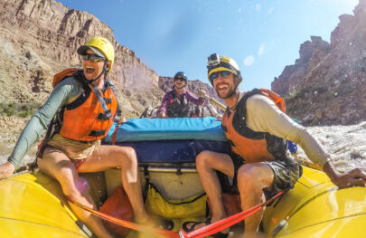 Three people in a yellow raft navigating the Colorado River through Cataract Canyon.
