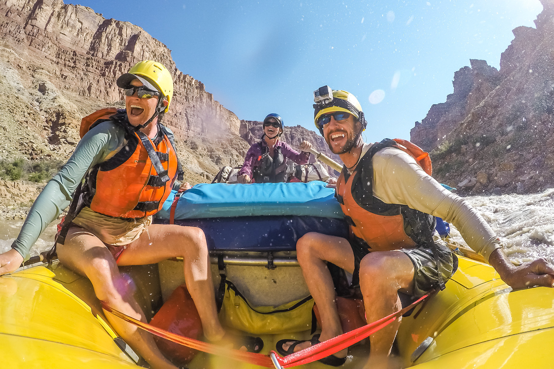 Three people in a yellow raft navigating the Colorado River through Cataract Canyon.