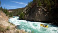 A yellow raft navigates a stretch of rapids on a turquoise blue river frothing with whitewater.