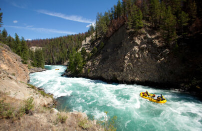 A yellow raft navigates a stretch of rapids on a turquoise blue river frothing with whitewater.