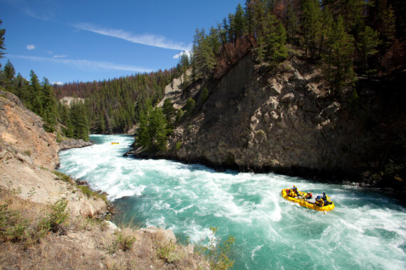 A yellow raft navigates a stretch of rapids on a turquoise blue river frothing with whitewater.