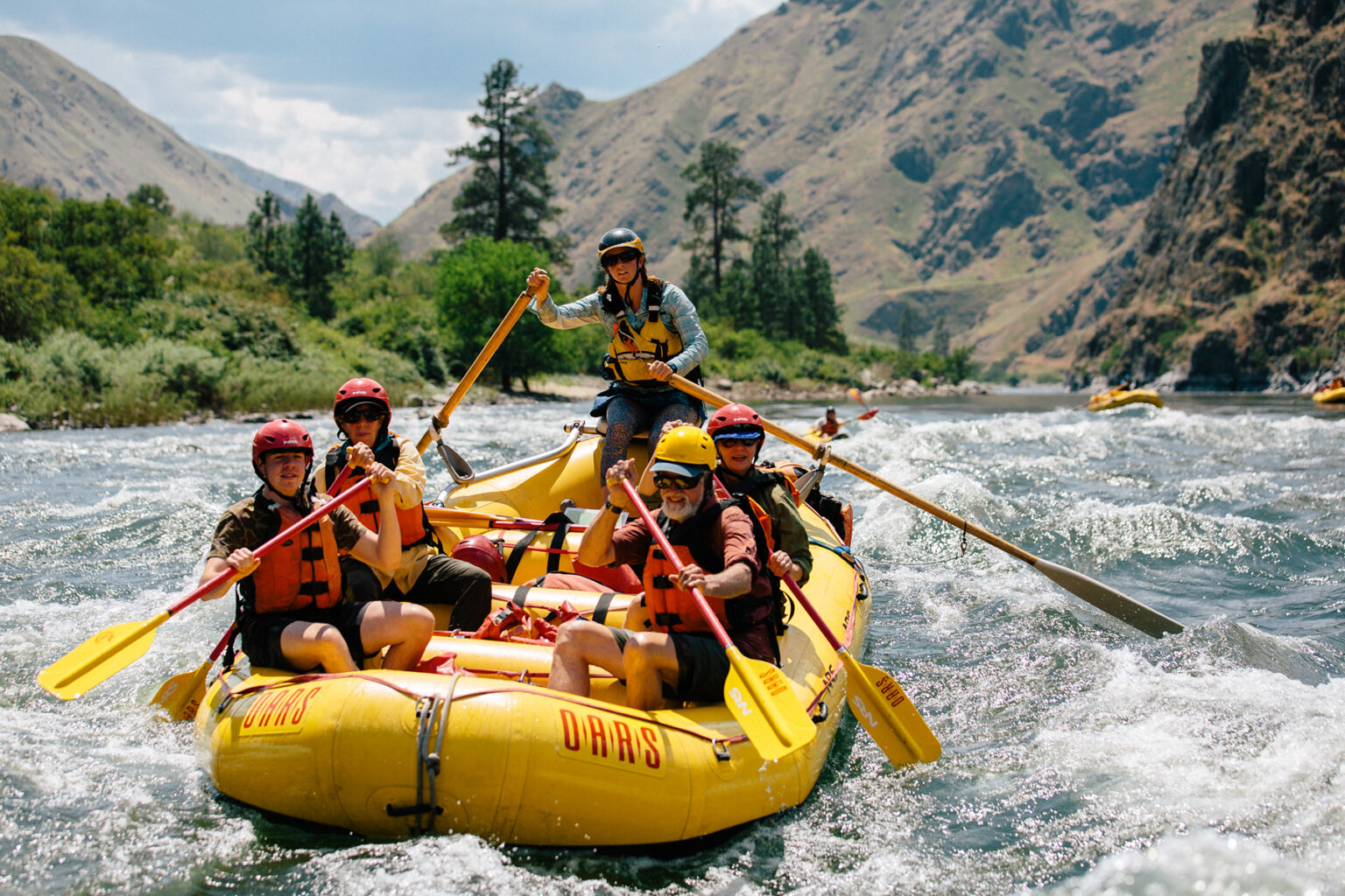 A group of people paddle through a rapid in a yellow raft on an OARS Snake River through Hells Canyon trip in Idaho.