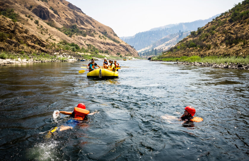 Two people swim in the Salmon River as a paddle boat with resting guests watch from upstream.