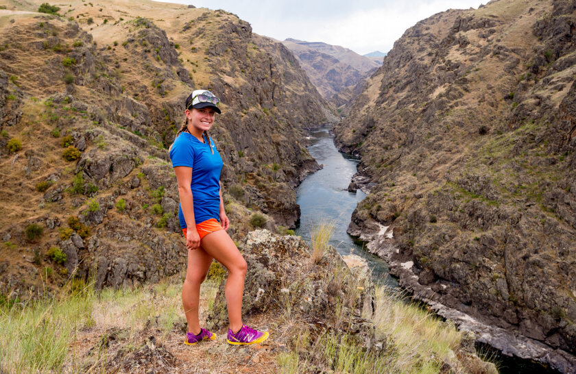 A hiker smiles for the camera standing high above the river with the Gorges of the Lower Salmon in the background.