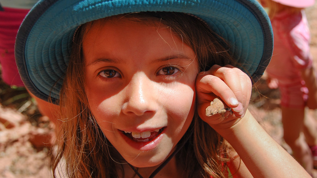 A girl wearing a hat holds a tiny desert frog in her hand that she discovered on an unplugged vacation 