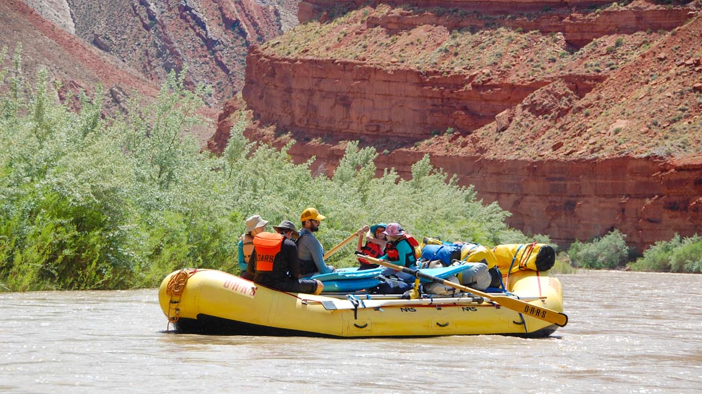 A family on an unplugged vacation float in a yellow raft down the San Juan River while the kids try their hand at rowing the boat