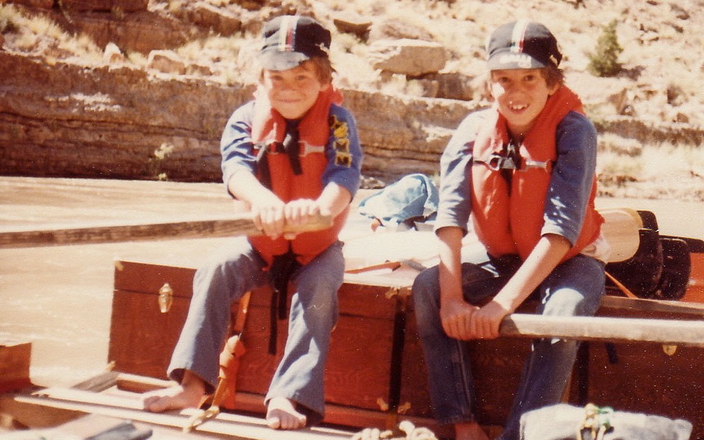 A vintage photo of two boys in life jackets rowing a raft on a desert river