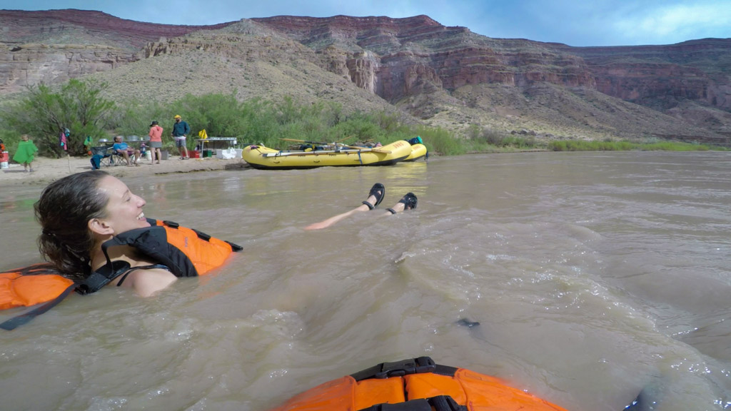 A woman wearing a PDF swims in the current of a river while people watch from shore