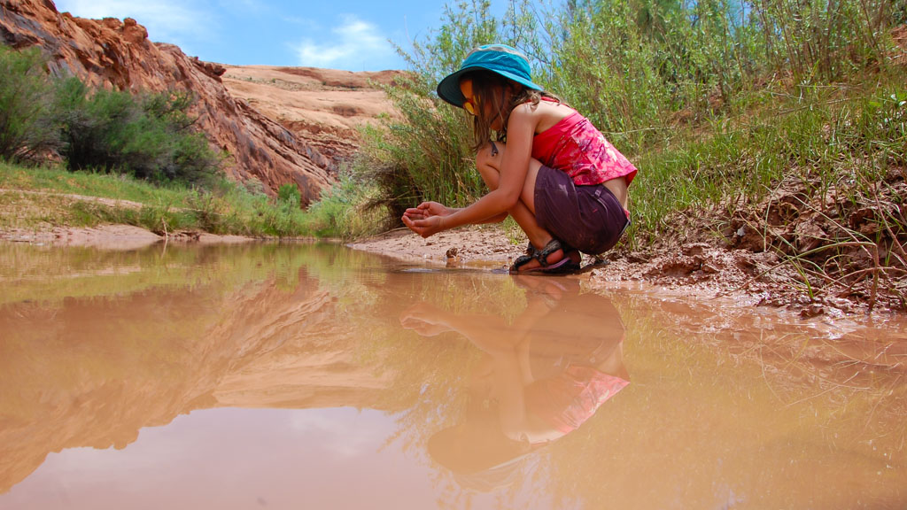 A girl searches for fish in a brown side stream 