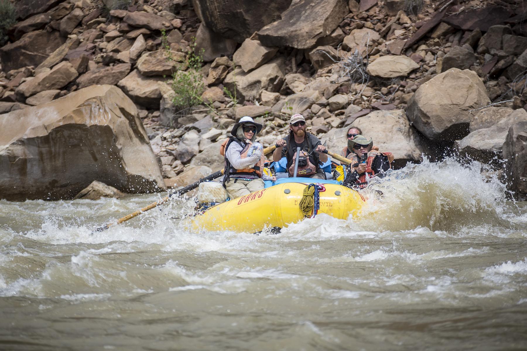 Three guests and a guide in an OARS raft going through a small rapid on the Green River through Desolation Canyon in Utah.