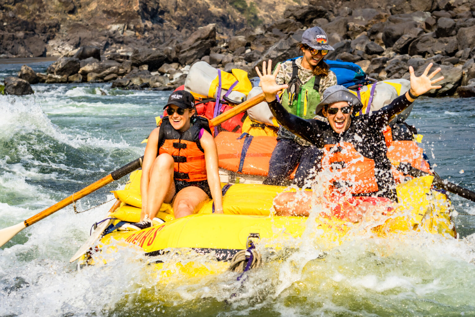 Three people in a yellow raft going through a rapid on the Lower Salmon River with big smiles on their faces.