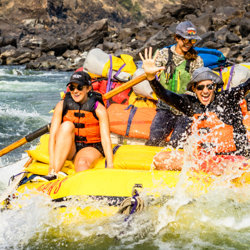 Three people in a yellow raft going through a rapid on the Lower Salmon River with big smiles on their faces.
