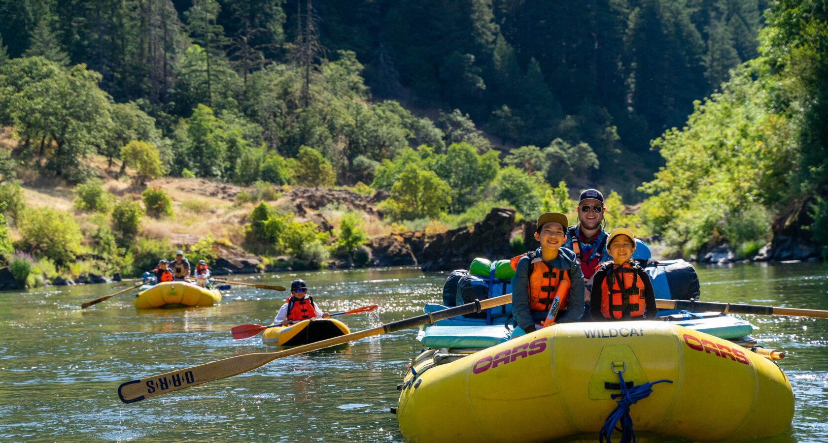 Two kids sit on the front of a yellow raft as they float on a calm stretch of the Rogue River