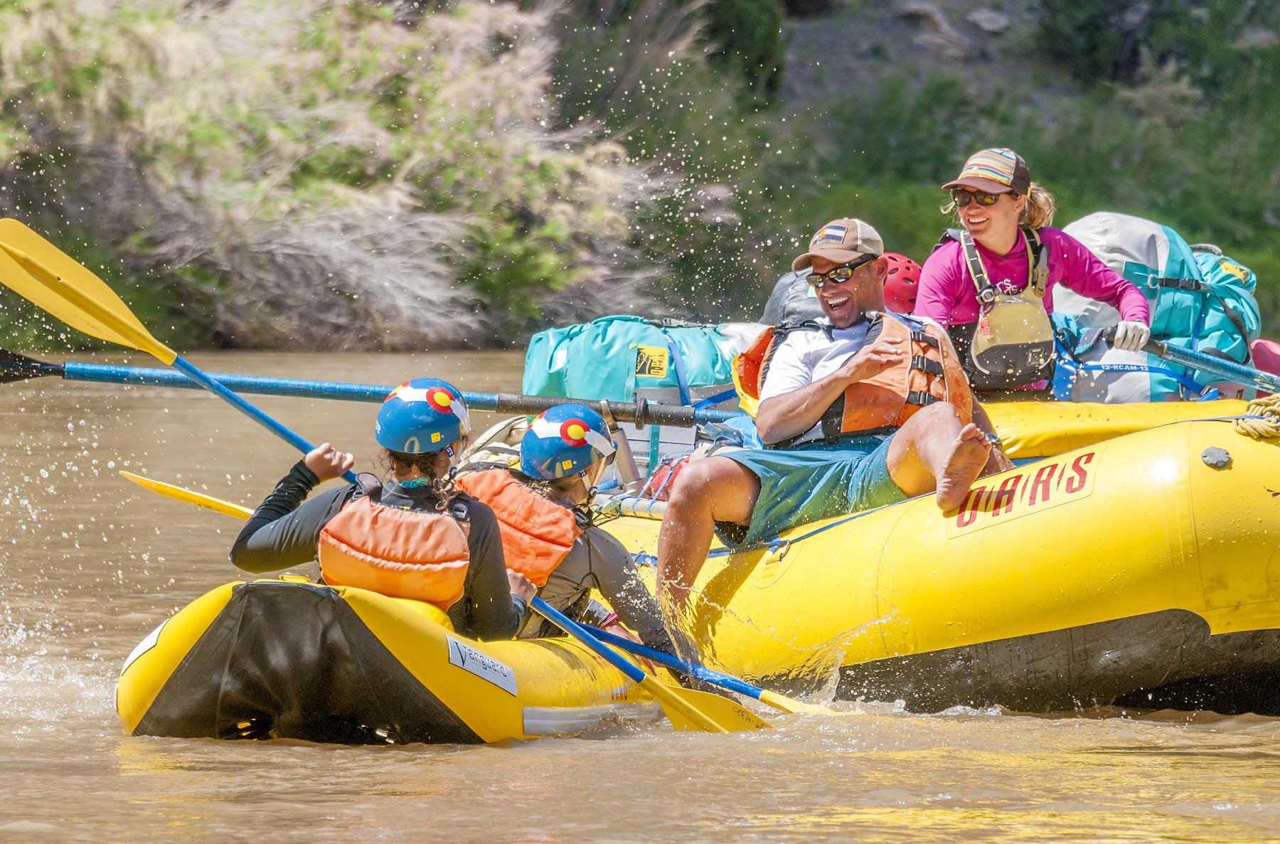 Three guests engage in a fun water fight on the Yampa River while a guide watches and smiles.