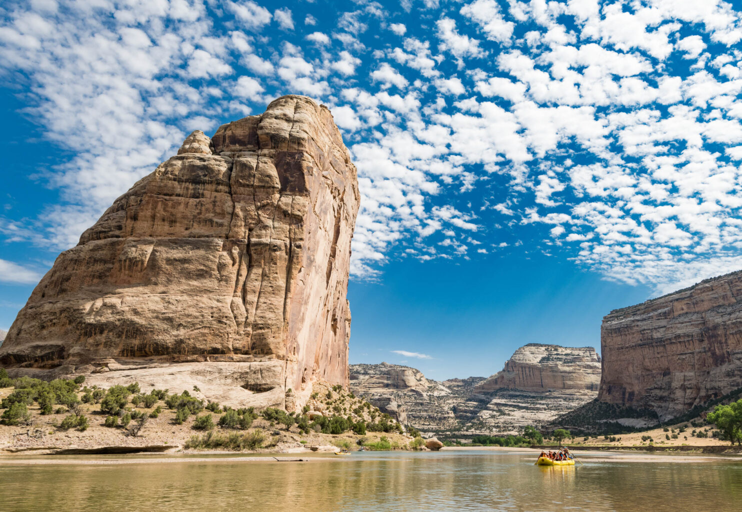 A yellow raft floats next to giant rock formation knowns at Steamboat Rock on the Green River