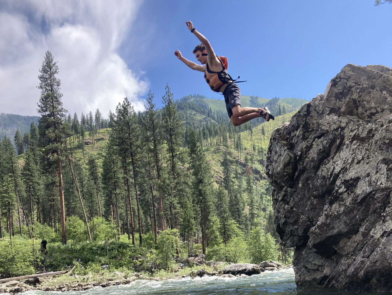A teenager leaps from a rock into the river below.