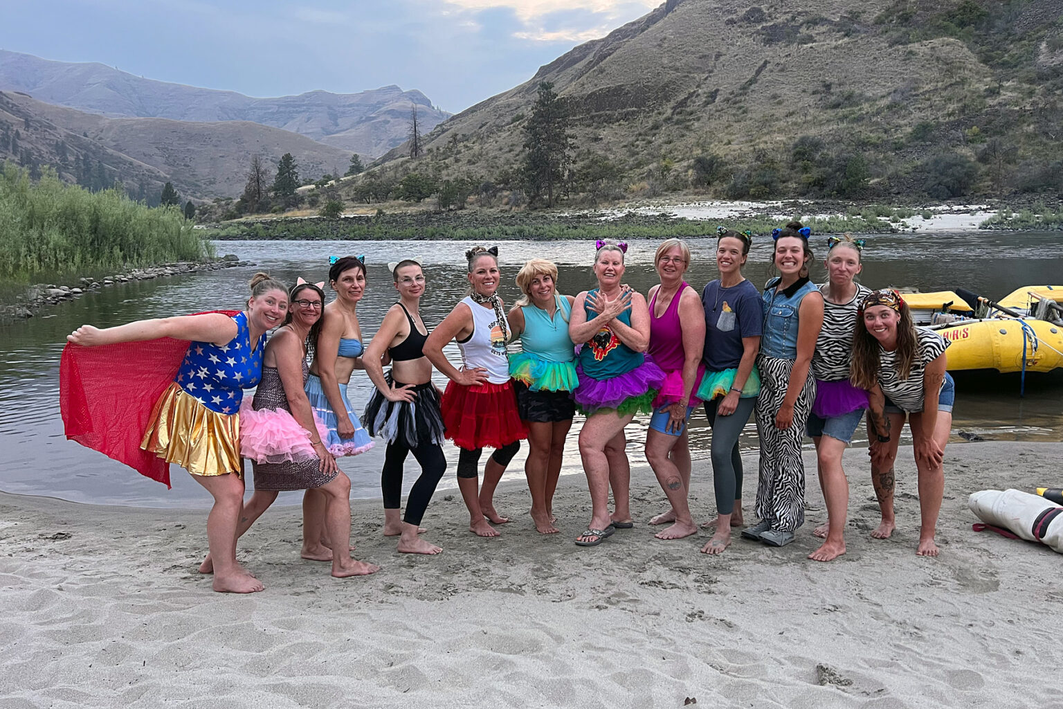 A group of smiling women in costumes lined up on a sandy beach on an OARS Gorges of the Lower Salmon River Women's Wellness trip.