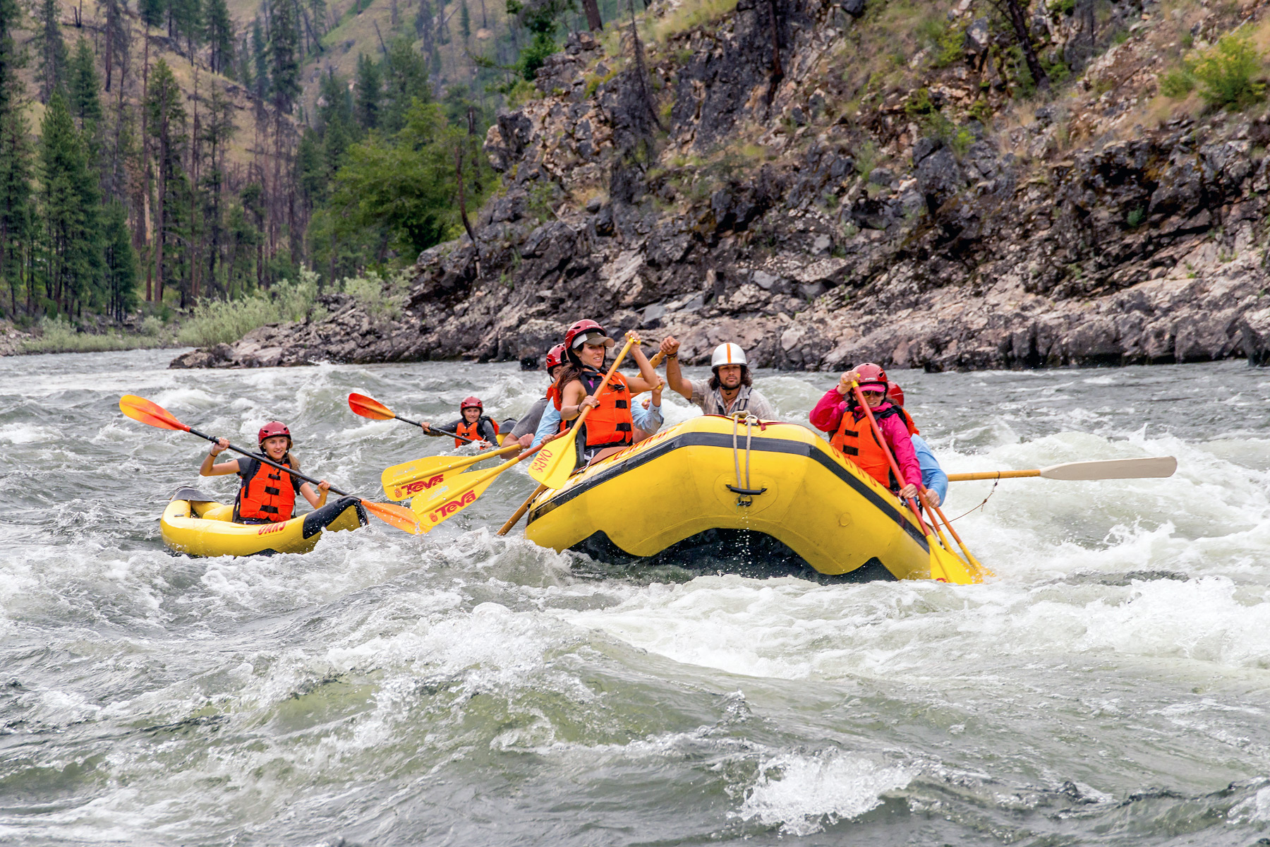 A paddle boat full of people and two solo kayakers take on a rapid on the Main Salmon River in Idaho.