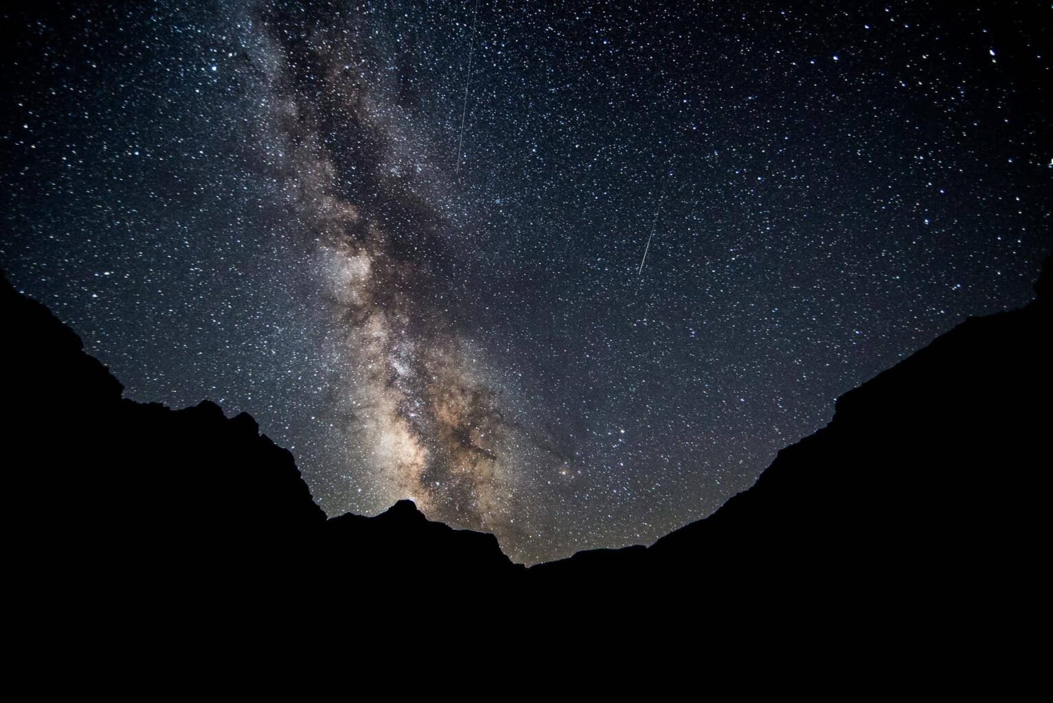 A vibrant Milky Way and starry sky above the outline of black canyon walls on an OARS river trip.