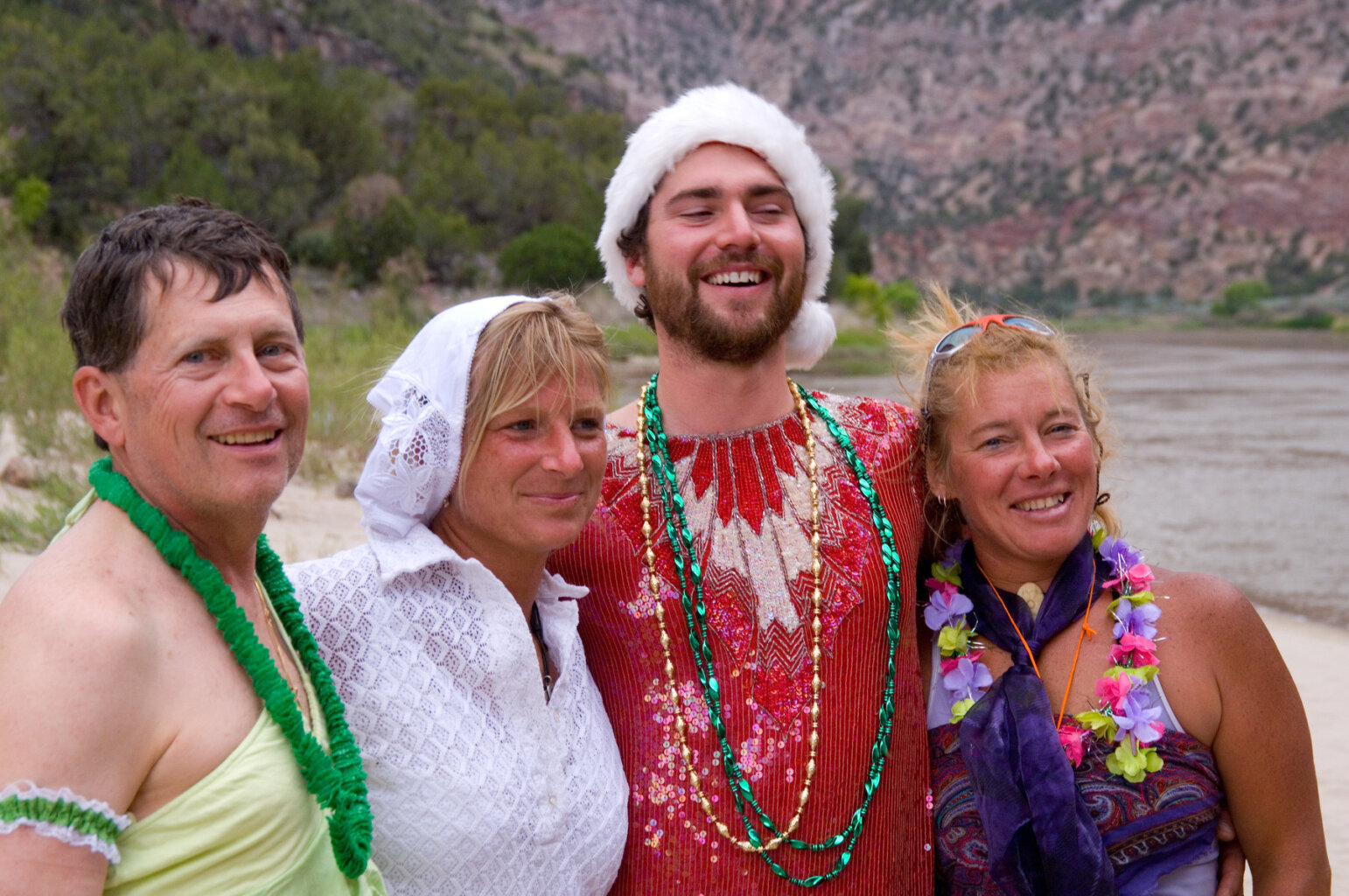 Four people smile and pose for the camera in costumes while at camp on a river trip.
