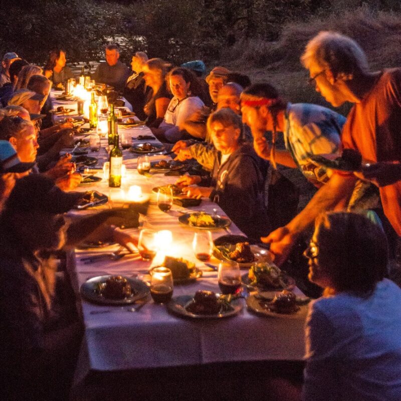 A group of people sit around a long candlelit table to enjoy a gourmet meal on an OARS Wine on the River trip.