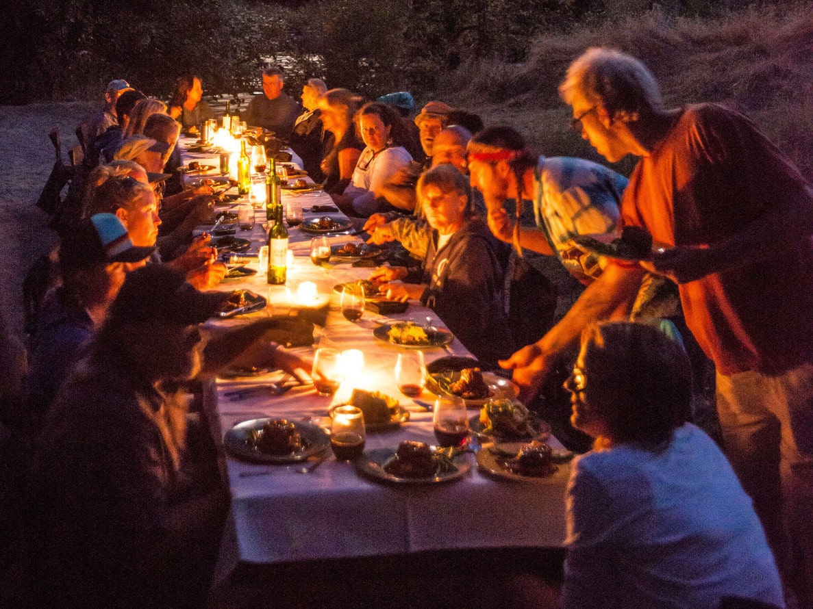 A group of people sit around a long candlelit table to enjoy a gourmet meal on an OARS Wine on the River trip.