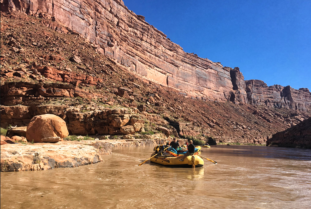 A single yellow raft floats down the San Juan River with several passengers