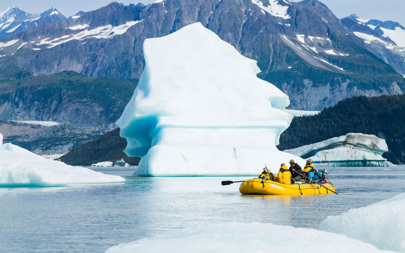 A yellow raft floats in front of a massive iceberg on a Tatshenshini rafting trip 