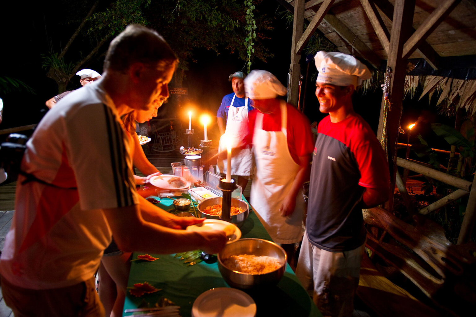 A chef smiles as he stands behind a buffet line and guests plate their dinners.