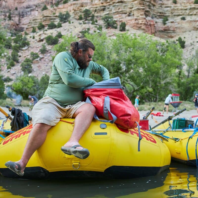 man reaching into a pack sitting on the front of a yellow raft.