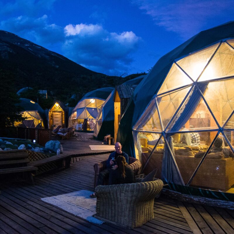 people sitting outside of large dome tents at dusk.