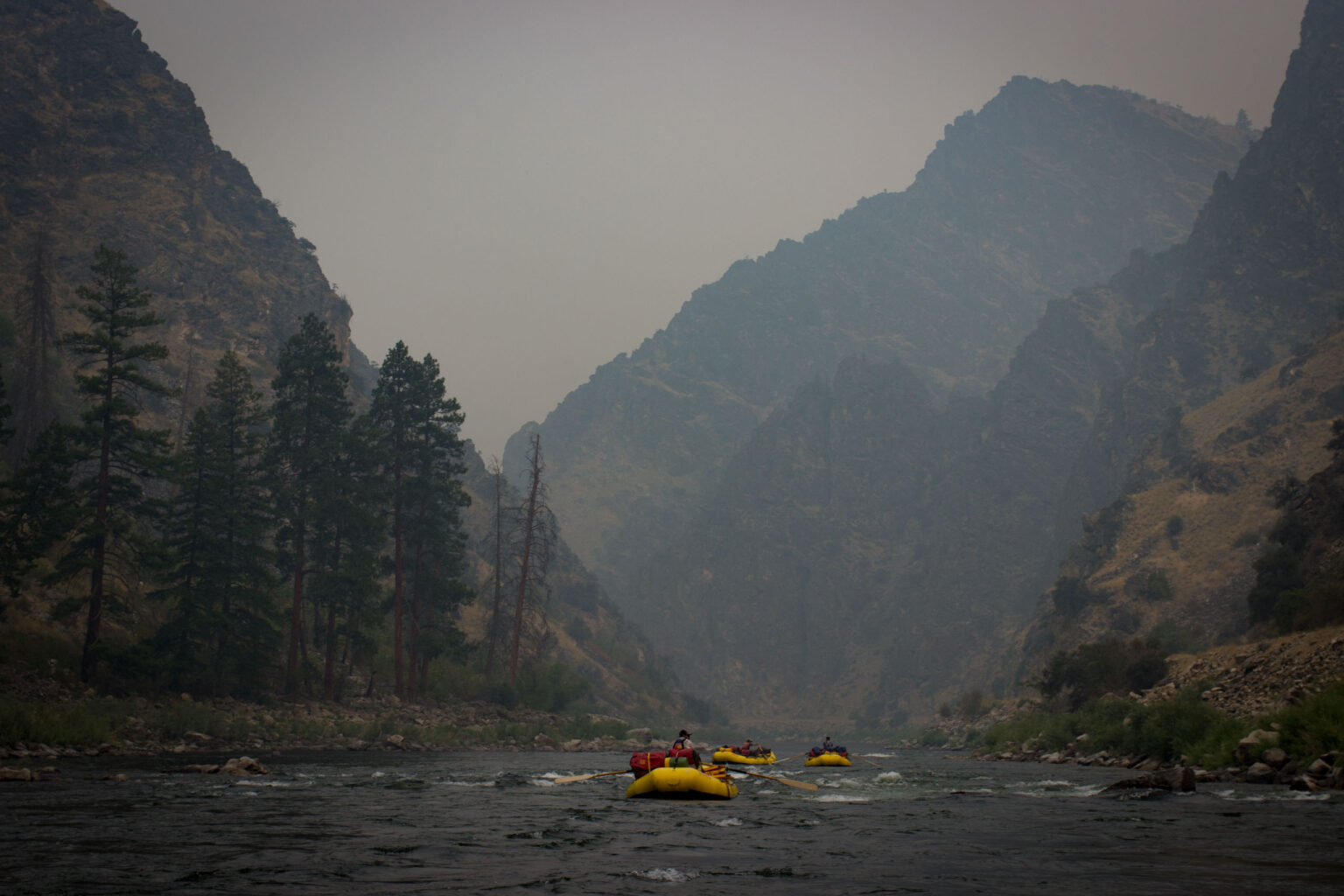 hazy sky over a river with a raft rowing down.