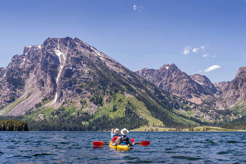 Two kayakers paddling on Jackson Lake in Grand Teton National Park with mountainous scenery in the background