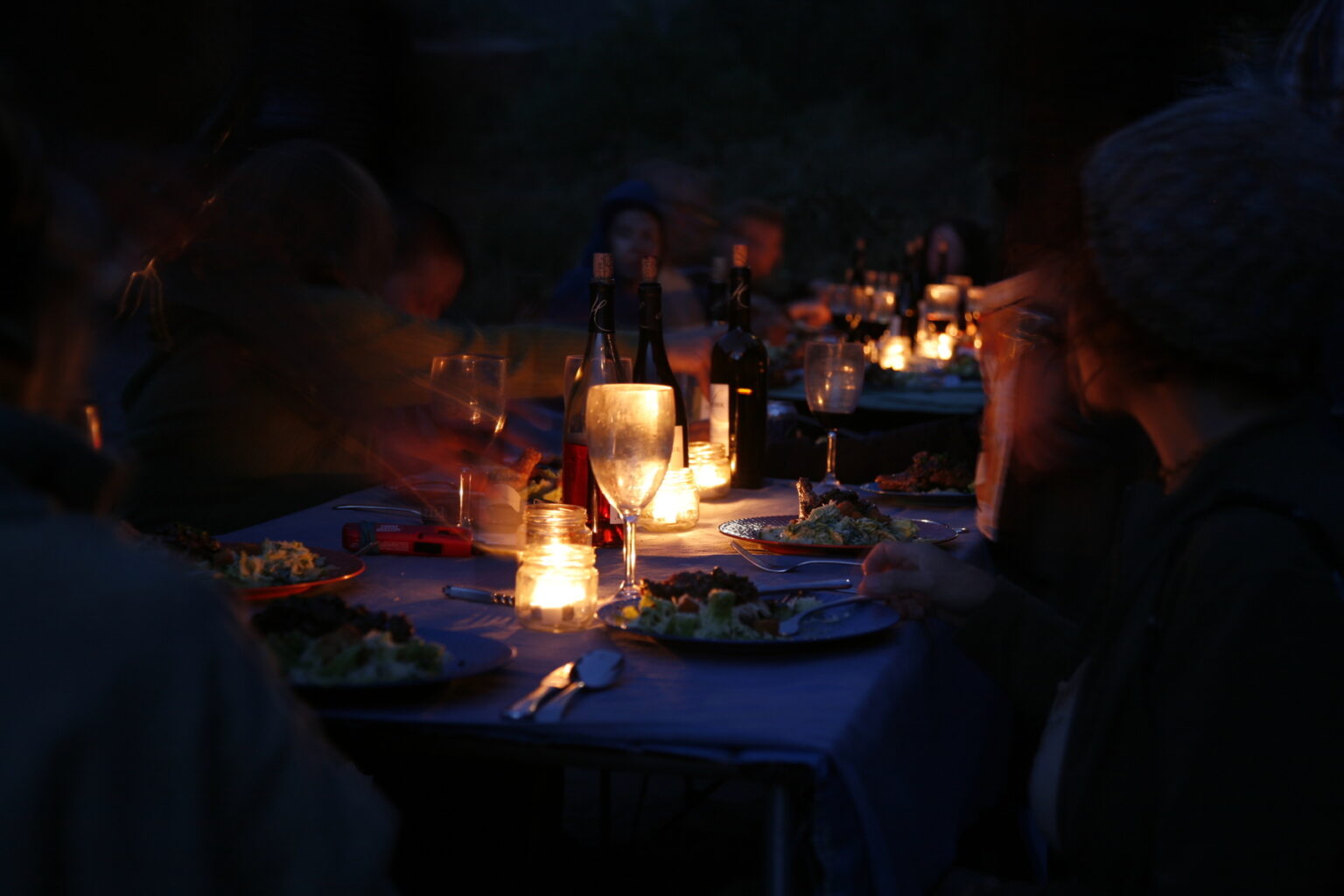 A group of people sit around a candlelit table enjoying a gourmet dinner on an OARS Rogue River Wilderness Gourmet trip.