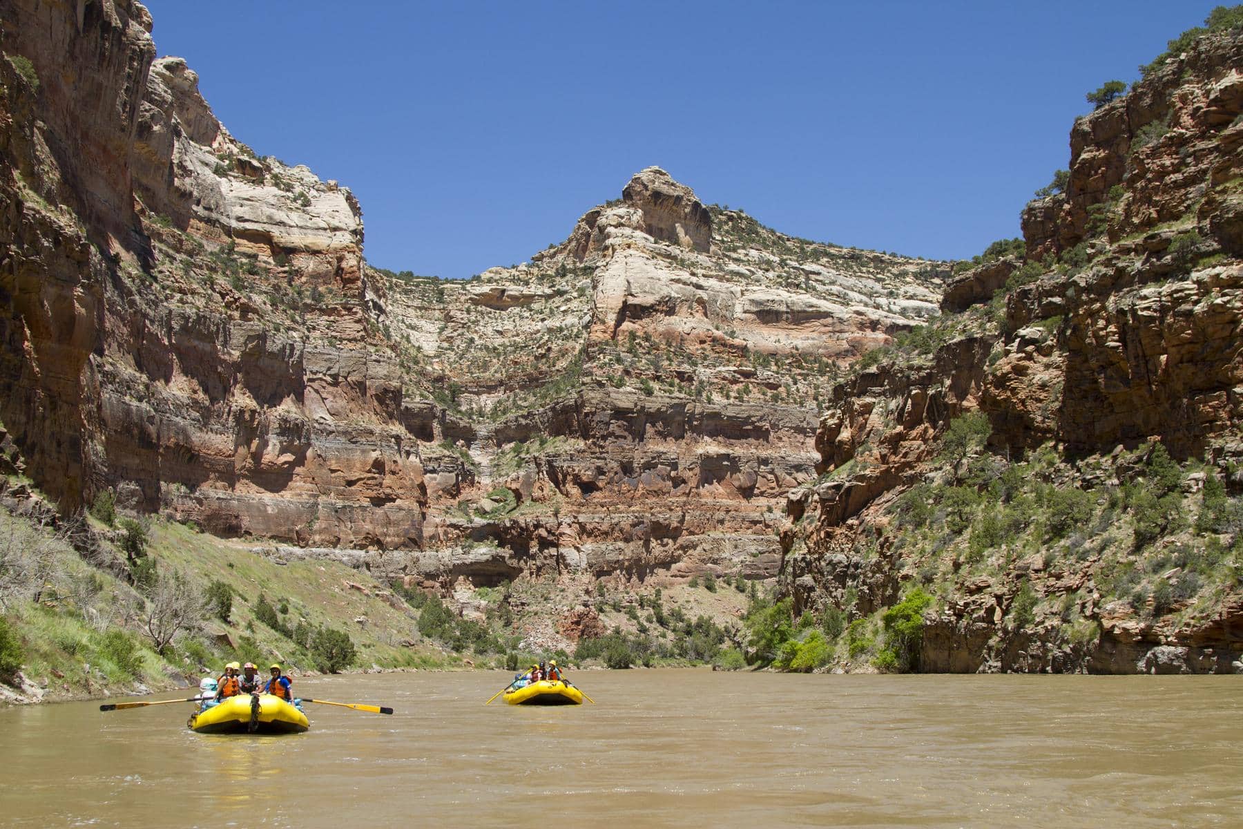 Two yellow OARS rafts full of people float down the Yampa River through a deep canyon in Dinosaur National Monument, Utah.