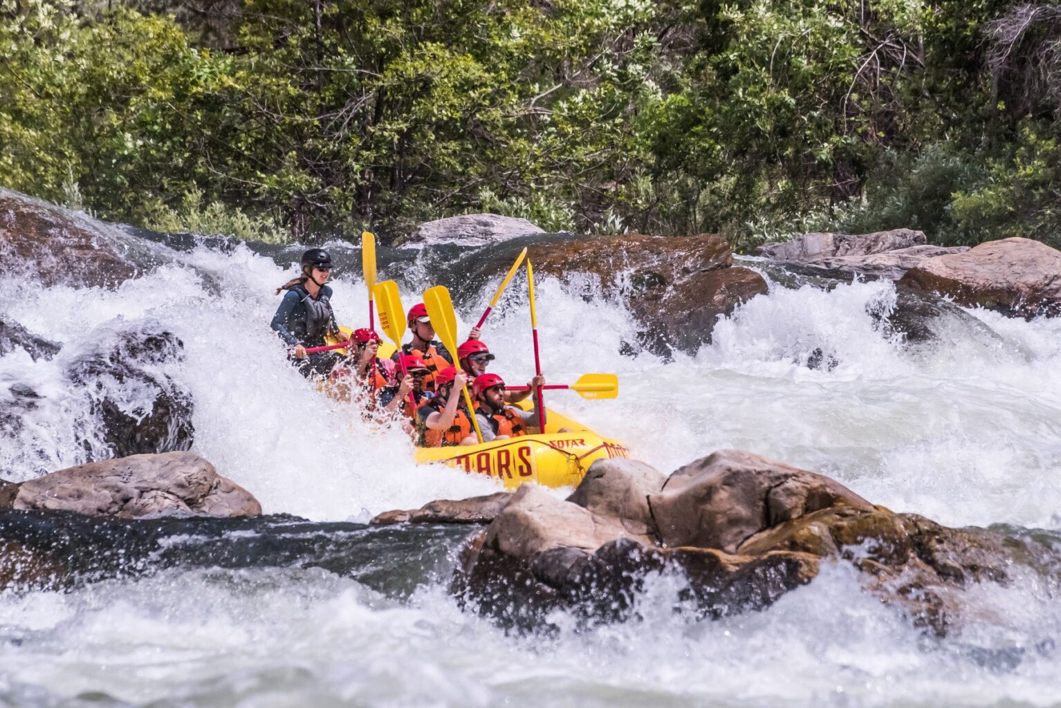 A group of people hold their paddles straight up in the air as they go down a rapid on the Tuolumne River in California