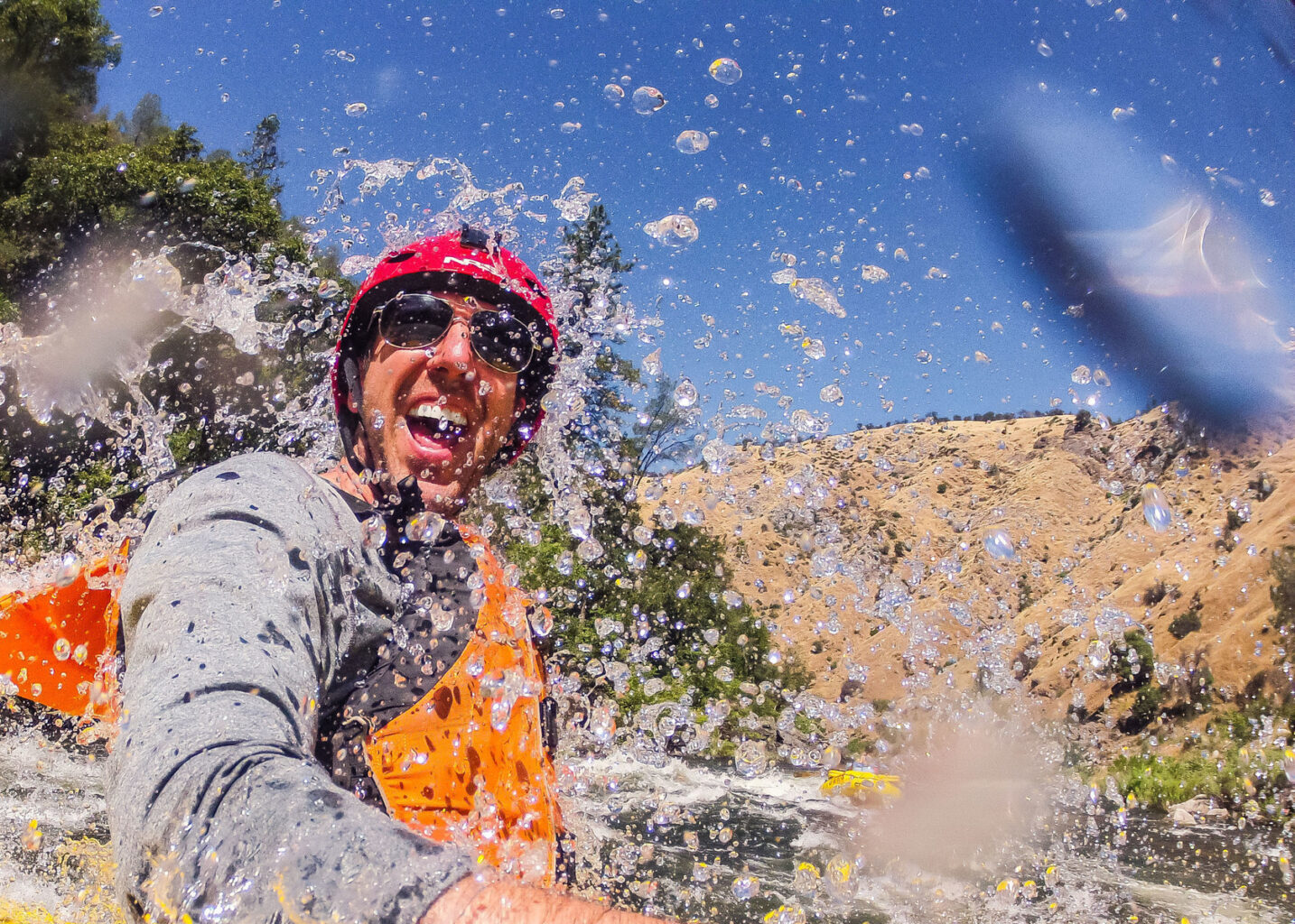 A laughing man getting splashed in the face by whitewater on the Tuolumne River in California.