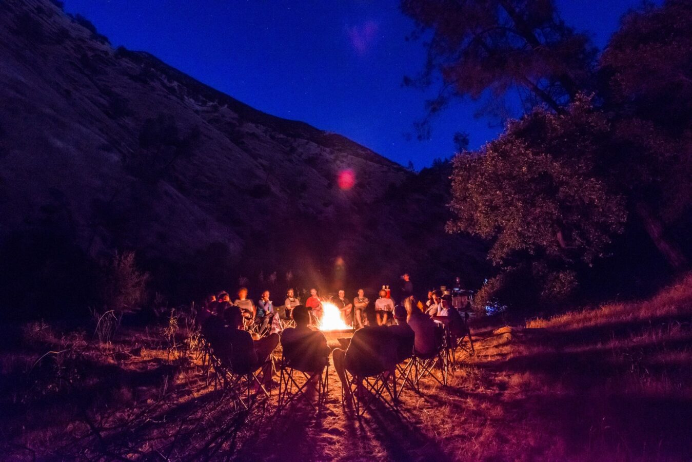 A group sits around a campfire in the chair circle at night on the Tuolumne River in California