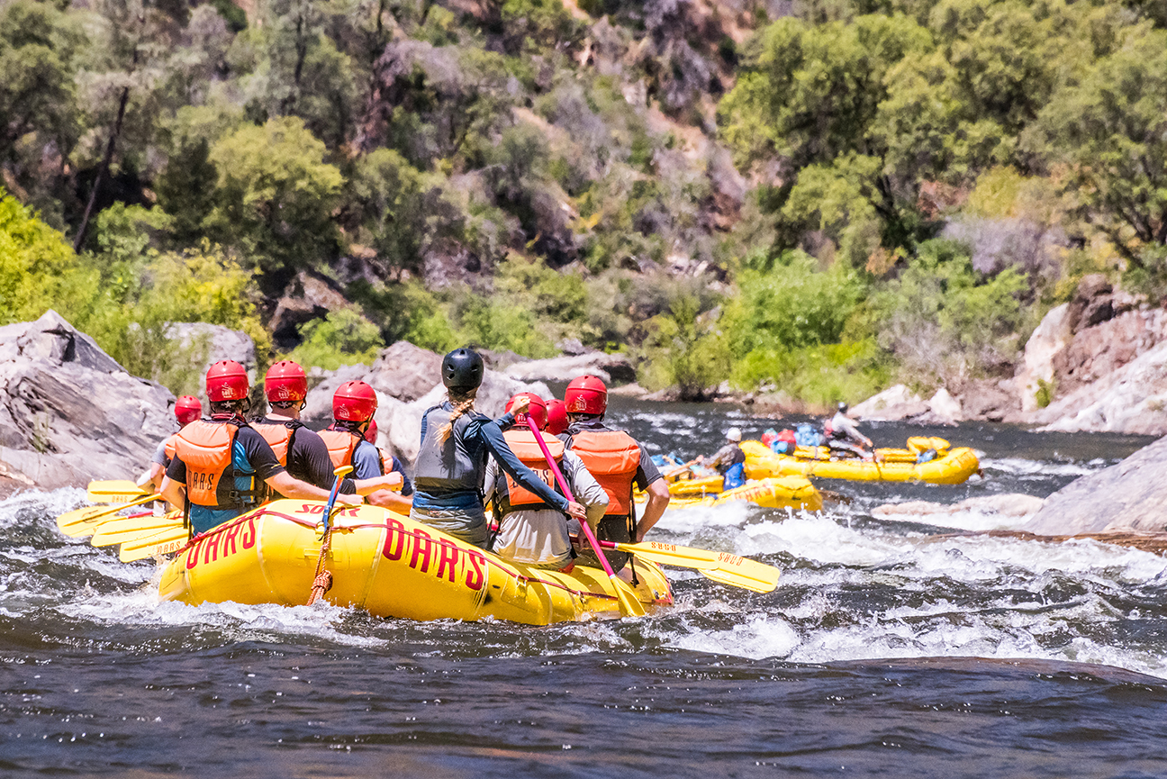 Shot from behind of multiple yellow boats on the Tuolumne River going through some light rapids