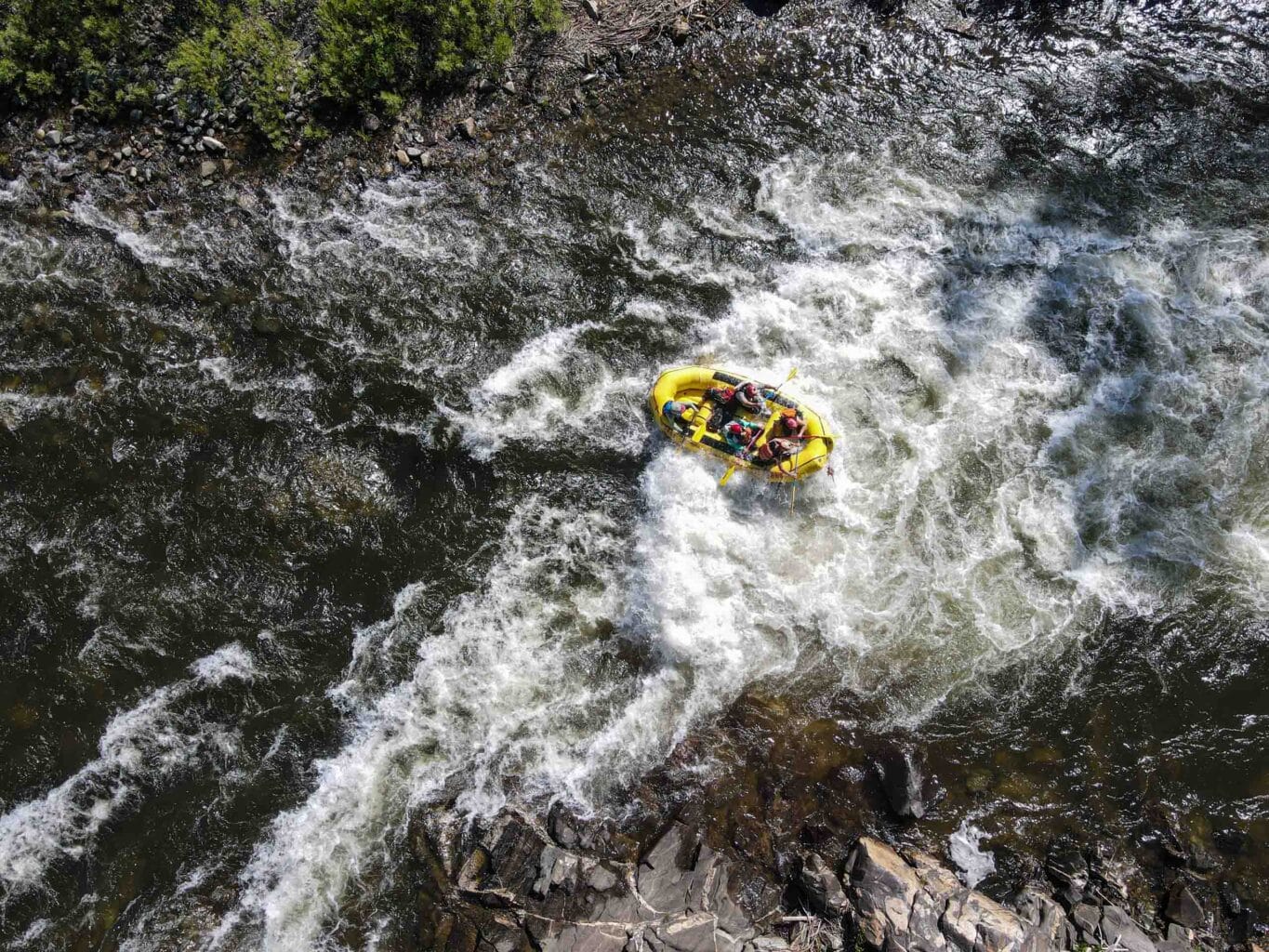 aerial shot of a raft in a river with rapids.