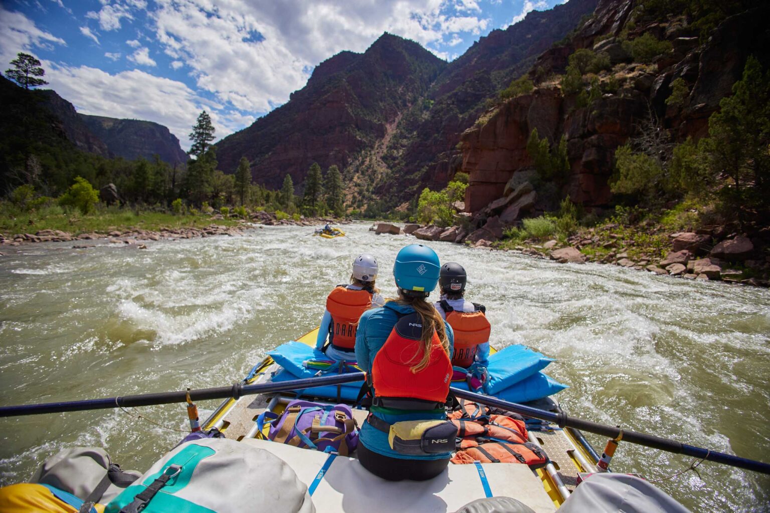 three people on a raft rowing through a choppy river.
