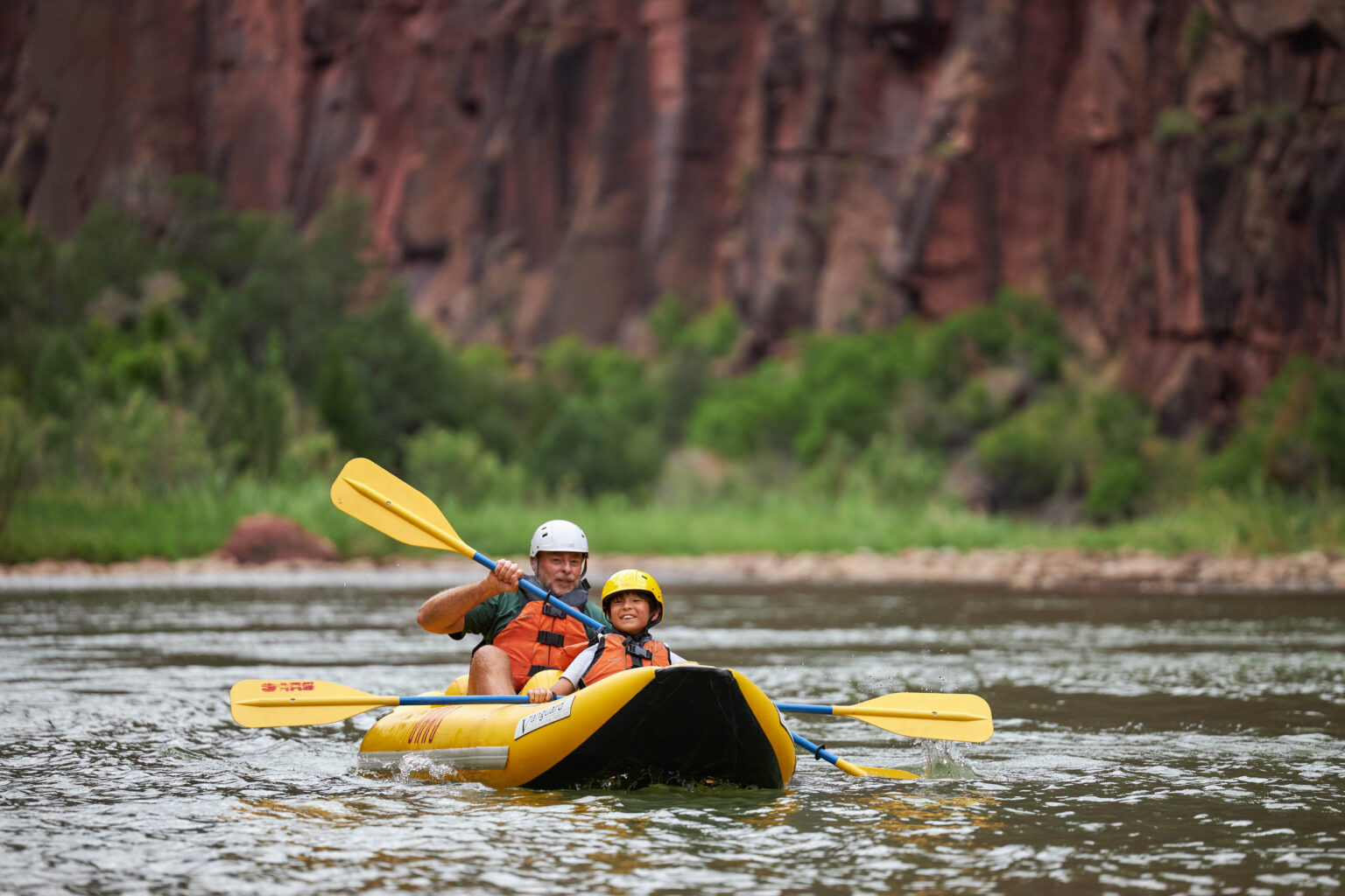 man and child rowing in a tandem kayak on a river.