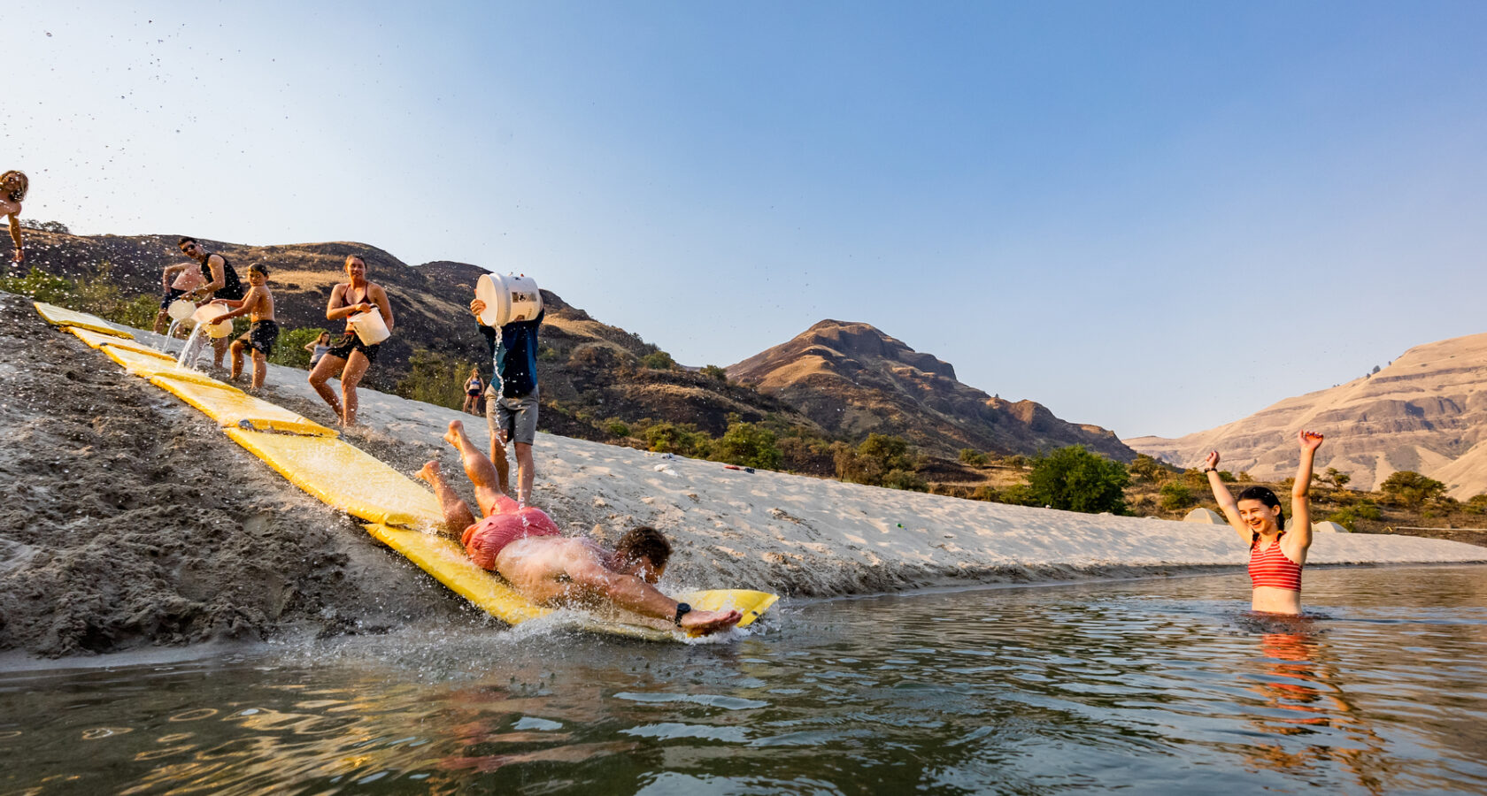 A man sliding down a a makeshift slip n' slide into a river