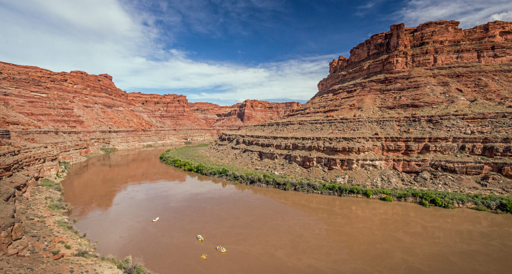 Aerial view of the Colorado River with several tiny, bright yellow rafts floating downstream