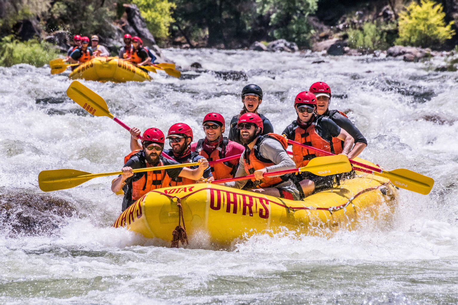 Two yellow boats full of people paddle through whitewater on the Tuolumne River in California.