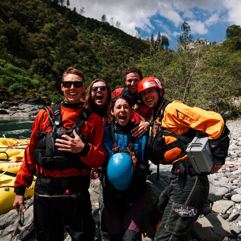 A group of river guides and trainees smile for a photo by the river