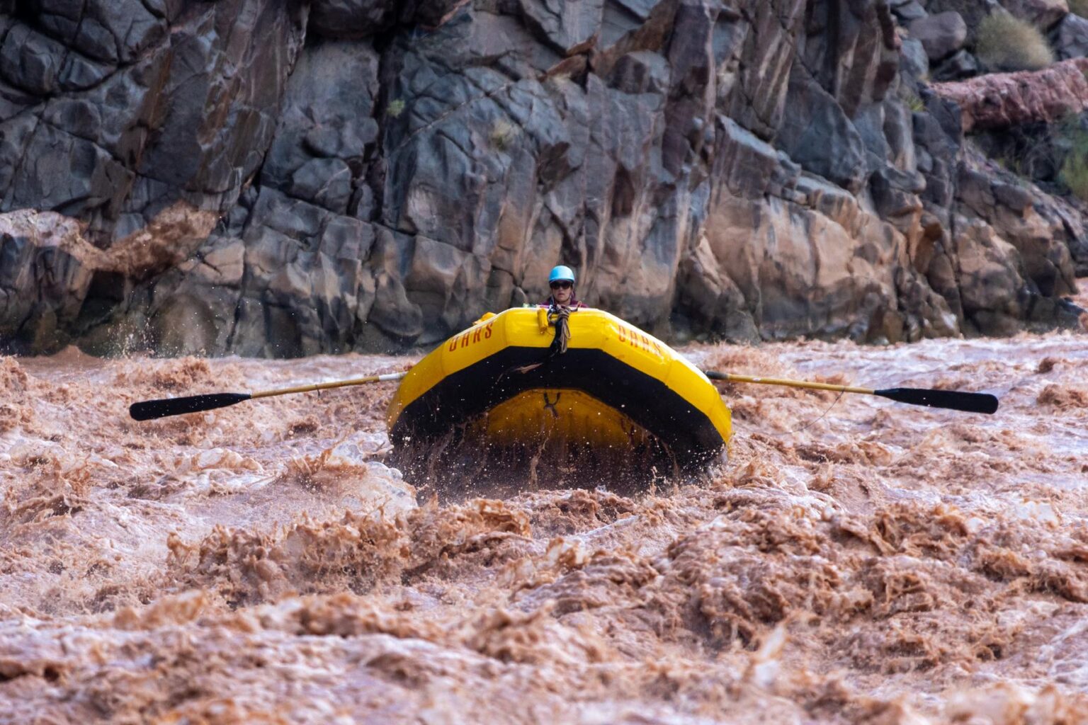 A river guide maneuvers a big yellow raft down the muddy waters of the Colorado River in Grand Canyon.